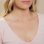 A close-up of a woman's neck wearing a white gold necklace with a letter Q charm. 