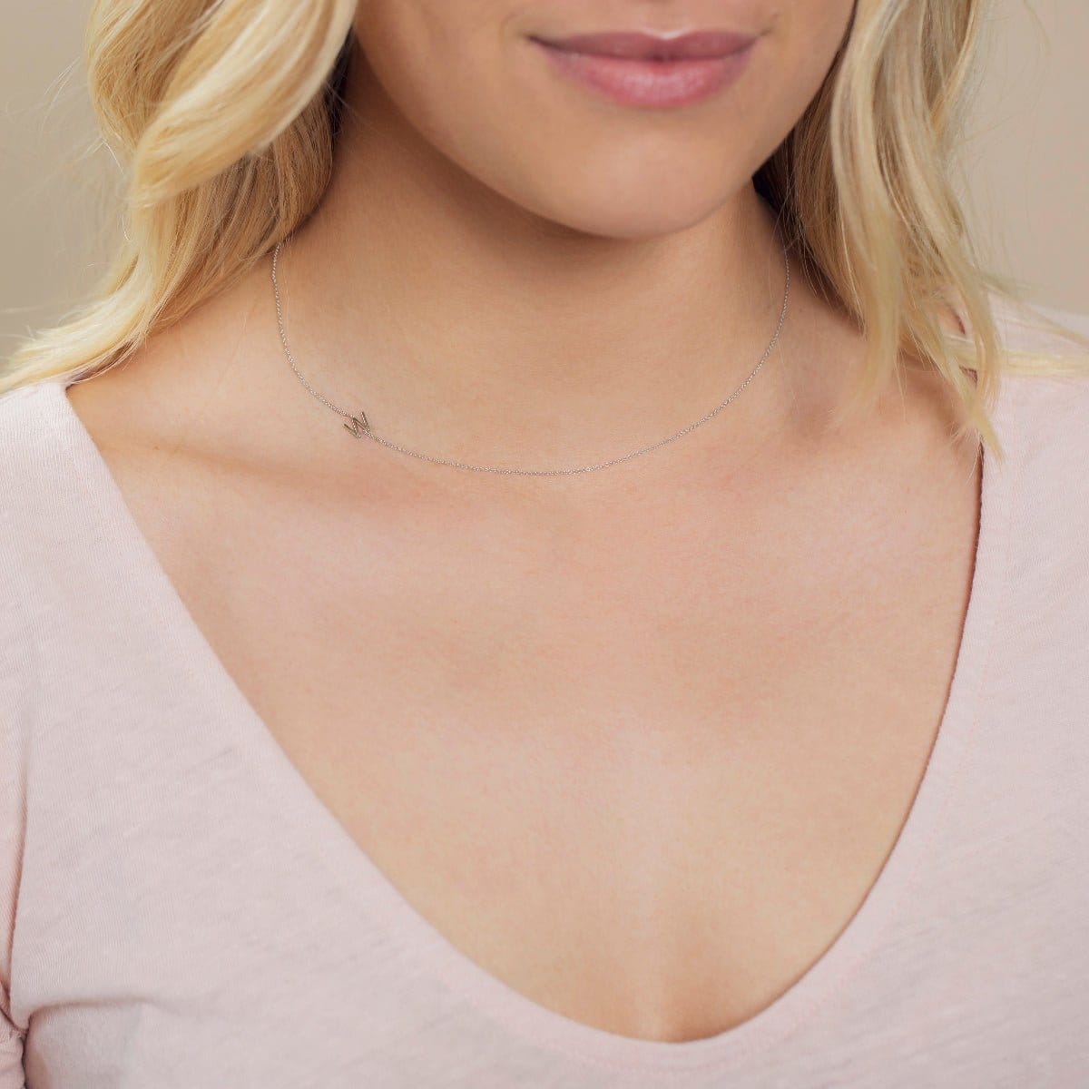 A close-up of a woman's neck wearing a white gold necklace with a letter W charm.