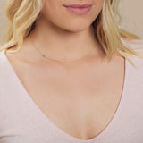 A close-up of a woman's neck wearing a white gold necklace with a letter X charm.