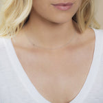 A close-up of a woman's neck wearing a 14k Gold Asymmetrical Number Necklace - 0 in white gold, with blonde hair, styled in a white top.