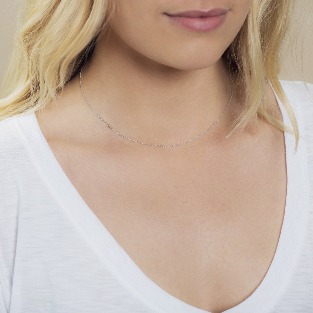 A close-up of a woman's neck wearing a white gold 14k Gold Asymmetrical Number Necklace - 1, with blonde hair and styled in a white top. 