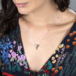 Close-up of a brunette woman's décolletage wearing a white gold Sharktooth Necklace with a navy top featuring flowers in various colours against a grey background. 