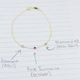 A yellow gold Custom Gold Bracelet with 3 letters and three birthstones (two diamonds and a pink tourmaline) displayed on a sheet of paper with annotations listing the birthstones and their corresponding months.