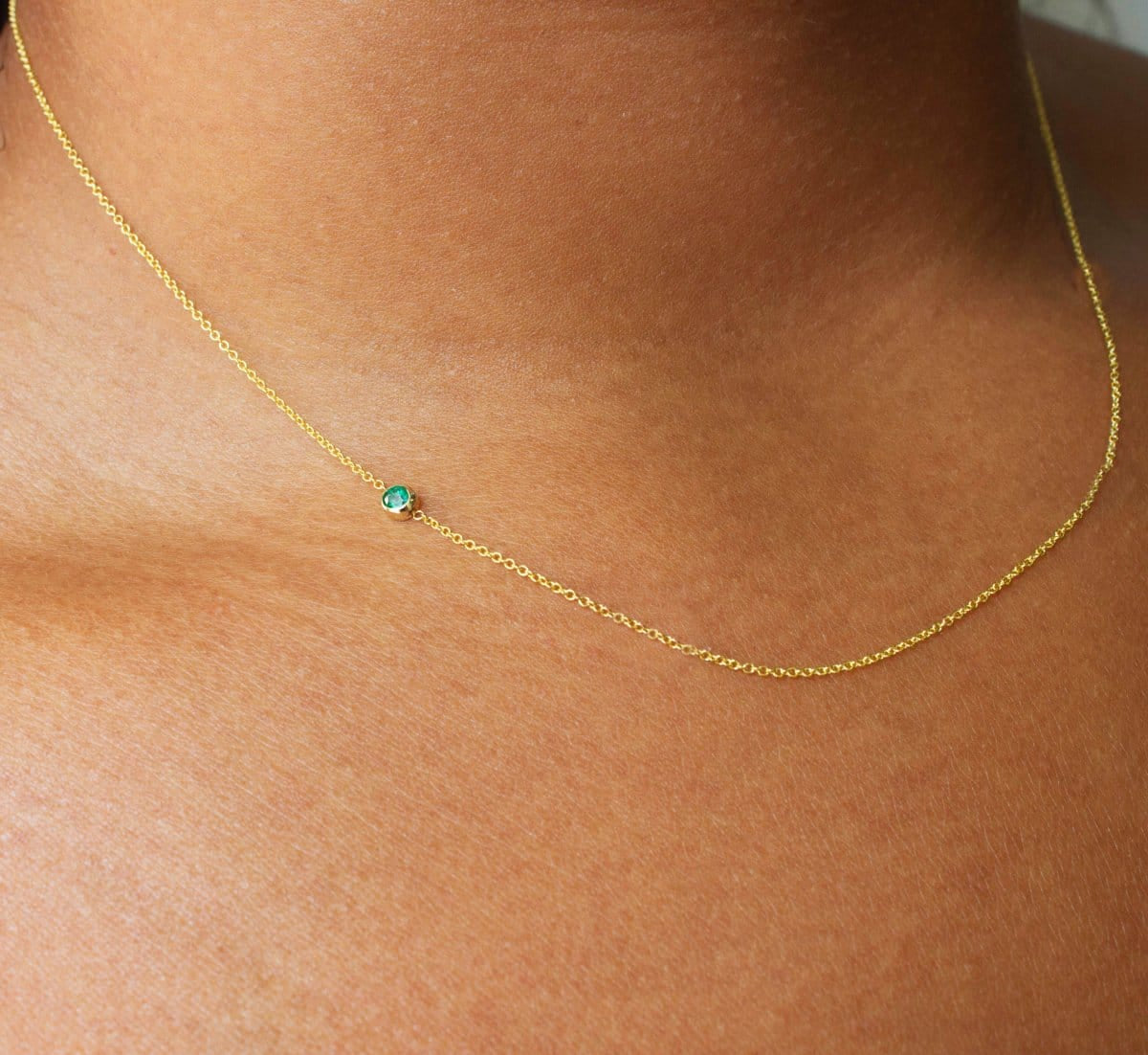A close up of a neck wearing a yellow gold 14K Gold Asymmetrical Birthstone Necklace - Emerald (May). 