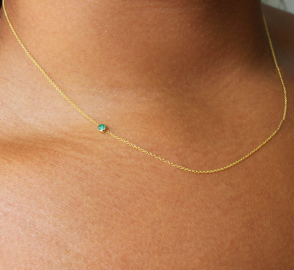 A close up of a neck wearing a yellow gold 14K Gold Asymmetrical Birthstone Necklace - Emerald (May). 
