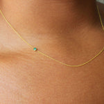 A close up of a neck wearing a yellow gold 14K Gold Asymmetrical Birthstone Necklace - Emerald (May). 