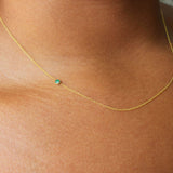 A close up of a neck wearing a yellow gold 14K Gold Asymmetrical Birthstone Necklace - Emerald (May). 
