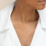 A close-up of a woman’s neck wearing yellow gold 14K Gold Asymmetrical Birthstone Necklace - Onyx (August), styled in a white shirt. 