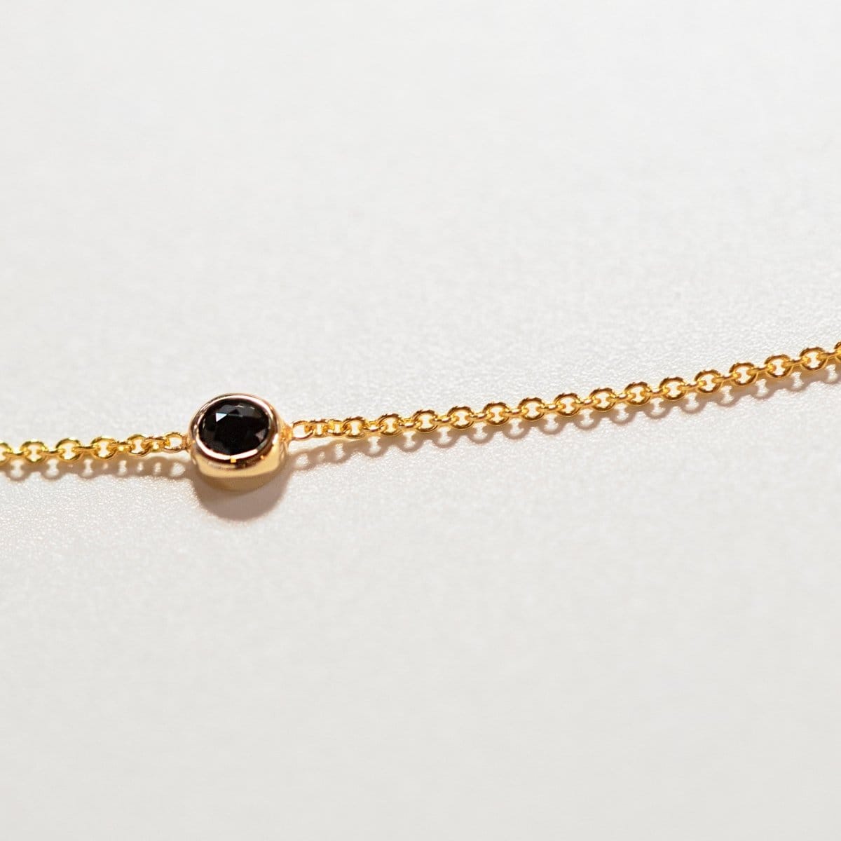 A yellow gold 14K Gold Asymmetrical Birthstone Necklace - Onyx (August) laid on a white surface. 