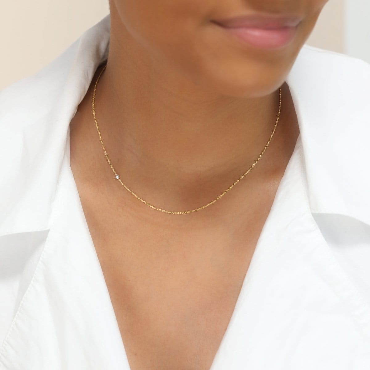 A woman’s neck wearing a yellow gold 14K Gold Asymmetrical Birthstone Necklace - Pearl (June), styled with a white shirt. 