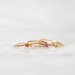 Four yellow gold Birthstone Rings (Citrine, Opal, Pink Tourmaline and Peridot) on a white background. 