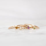 Four yellow gold Birthstone Rings (Citrine, Opal, Pink Tourmaline and Peridot) on a white background. 