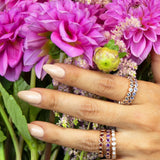 A hand wearing several Bouquet Rings with pink flowers in the background. 