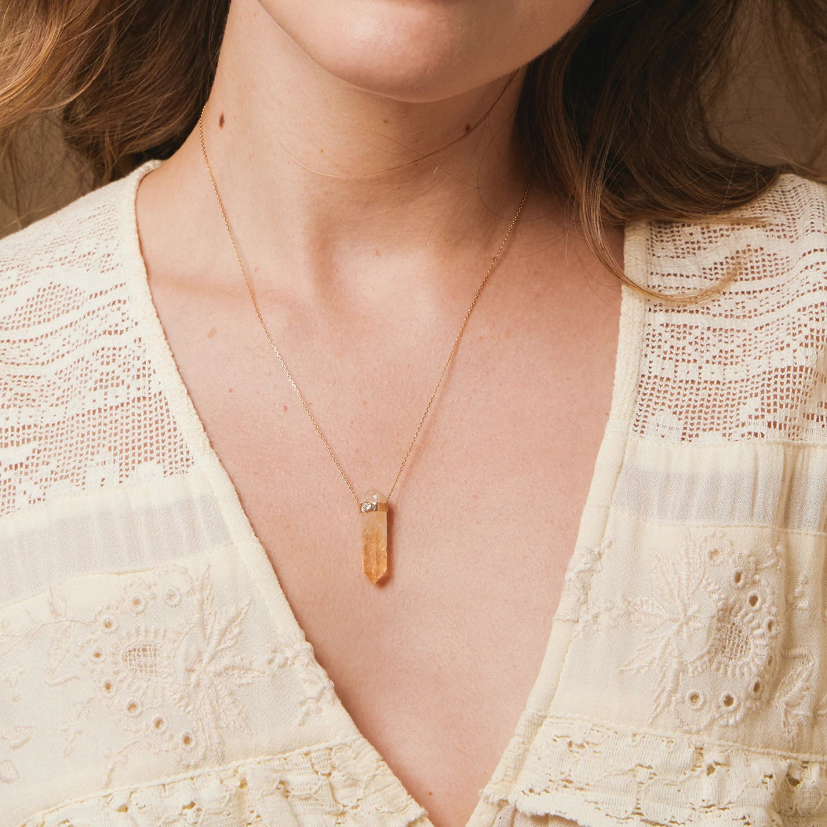 A close-up of a neck wearing The Happiness Retreat Necklace, styled in a low neck light yellow top. 