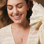 A woman wearing The Happiness Retreat Necklace, a Solid Eclipse Earring - Small and several rings, styled in a light yellow lace top with a warm background.