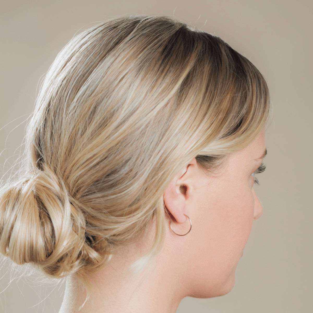 Side profile of a woman wearing a Crescent Hoop / Medium with her blonde hair in a bun against a neutral background. 