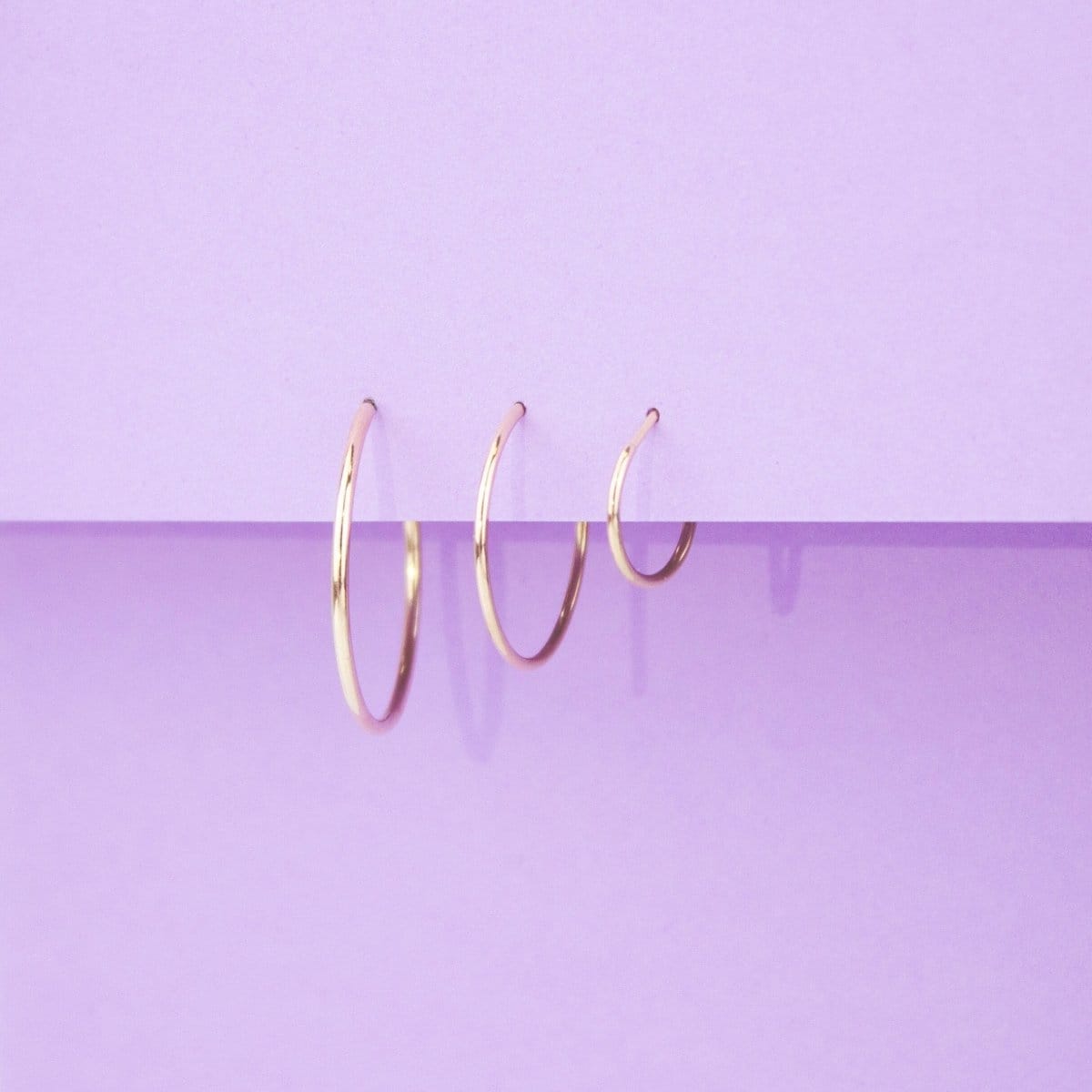 Yellow gold Crescent Hoops in large, medium and small on a purple background. 
