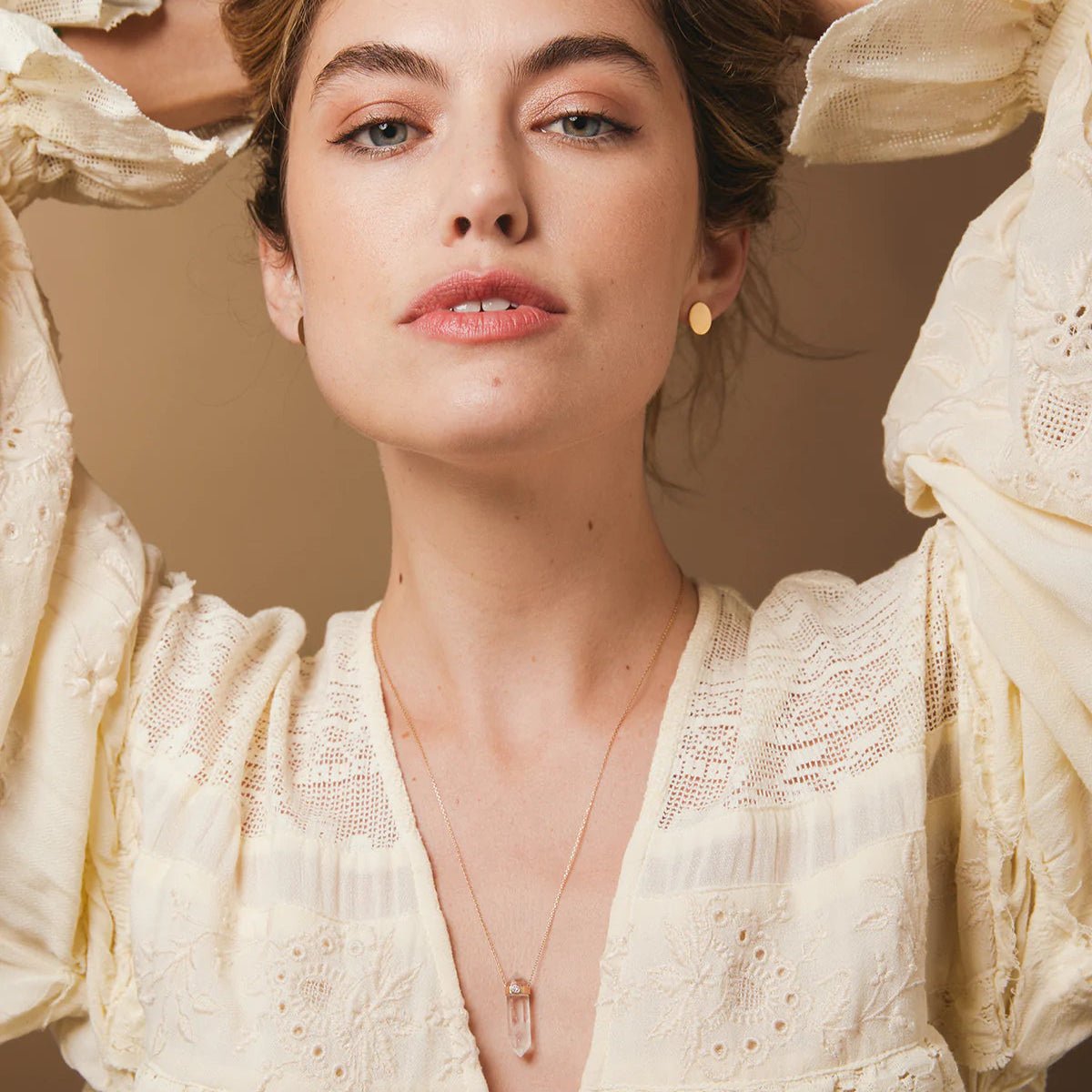 A woman wearing The Clarity Retreat Necklace and Solid Eclipse Earrings - Small, styled with a light yellow long sleeve top against a light brown background. 