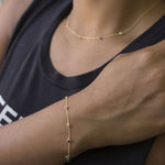 A close-up of an arm and neck wearing a Custom Gold Bracelet with four diamond birthstones and a Quintet Diamond Layering Necklace, with a black top with white writing. 