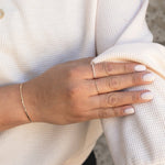 Close-up of a woman's hand wearing a Pave Diamond Ring, 4 Diamond Ring and an Off the Cuff Bracelet, styled with a white jumper. 