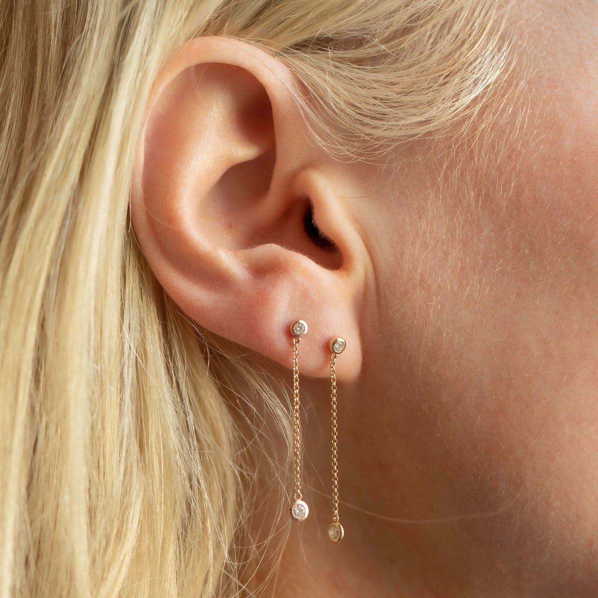Close-up of two yellow gold Droplet Diamond Earrings in a blonde woman's ear. 