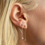 Close-up of two yellow gold Droplet Diamond Earrings in a blonde woman's ear. 