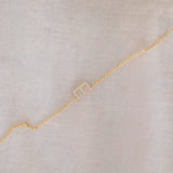 A yellow gold necklace with a letter E charm, displayed diagonally on a cream fabric background.