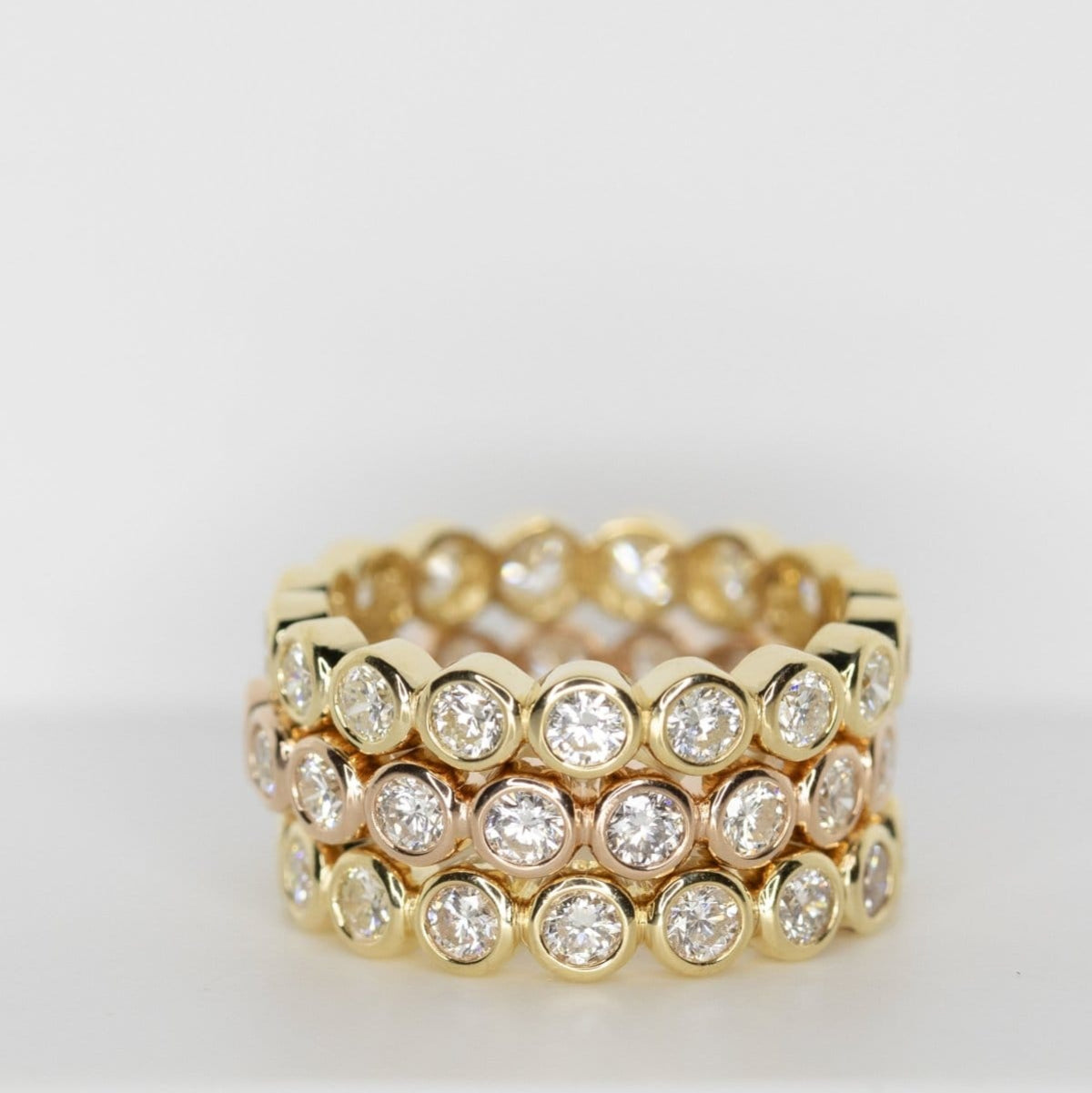 Three yellow gold The Evermore Rings against a light grey background.  