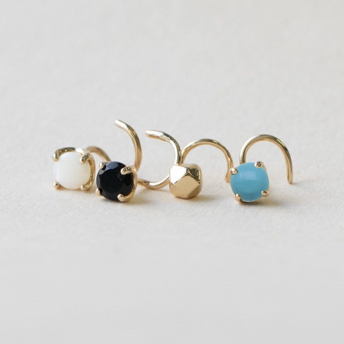 An Alli Webb Faceted Comfort Stud, Turquoise Comfort Stud, Opal Comfort Stud and Opal Comfort Stud on a light grey surface.