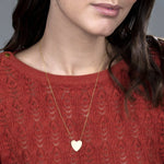 Close-up of a woman's décolletage wearing a Heart Necklace, with a red knit top and her brown hair visible. 