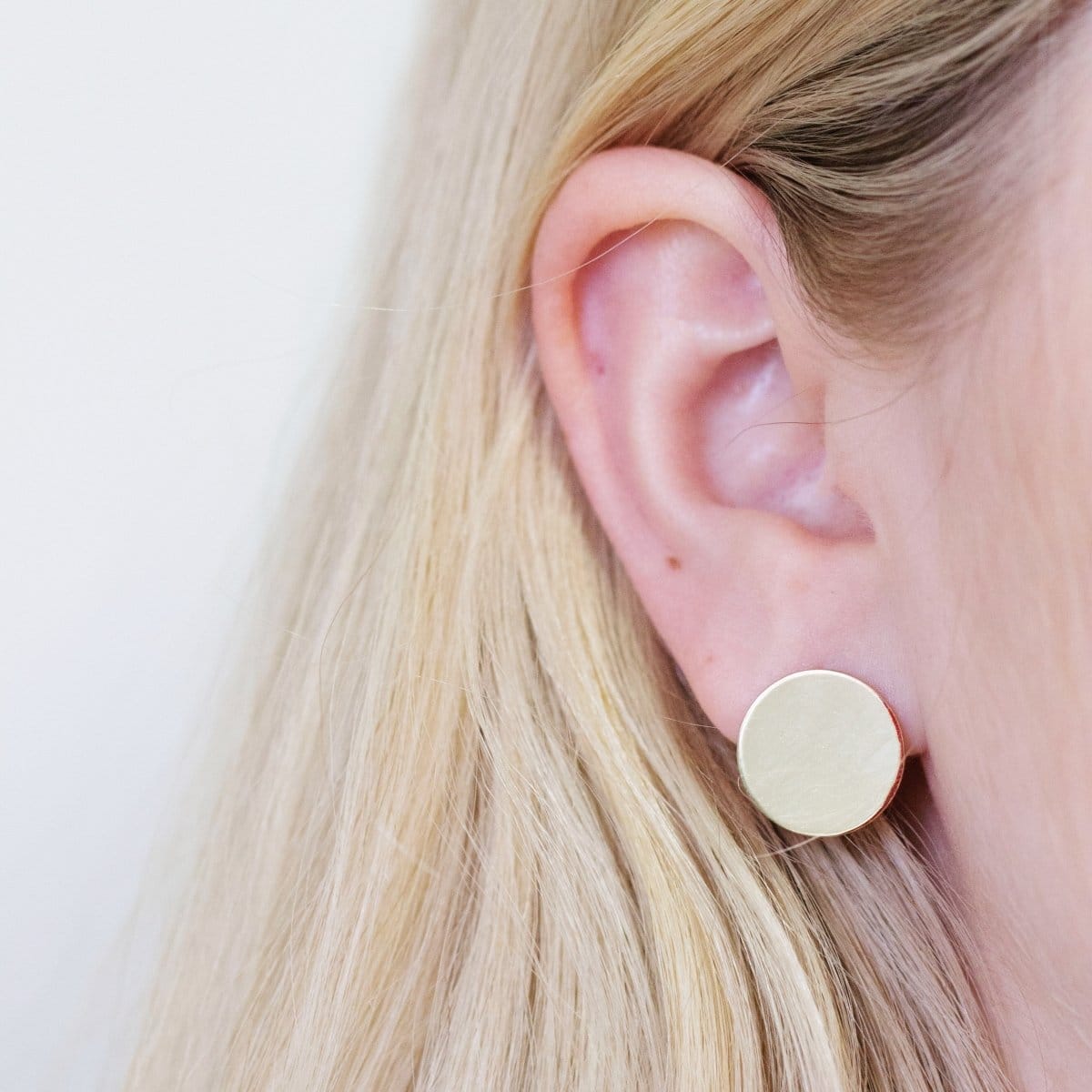 Close-up of a yellow gold Solid Eclipse Earring - Large in a blonde woman's ear against a white background. 