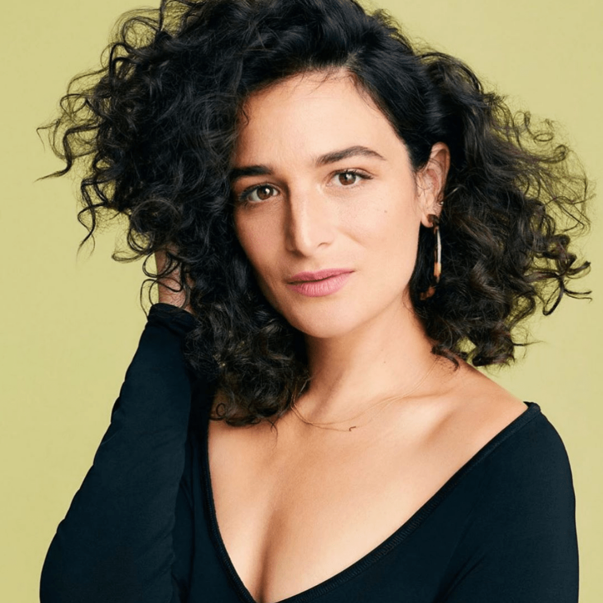 A woman with black curly hair wearing two gold necklaces, one with a letter J charm.
