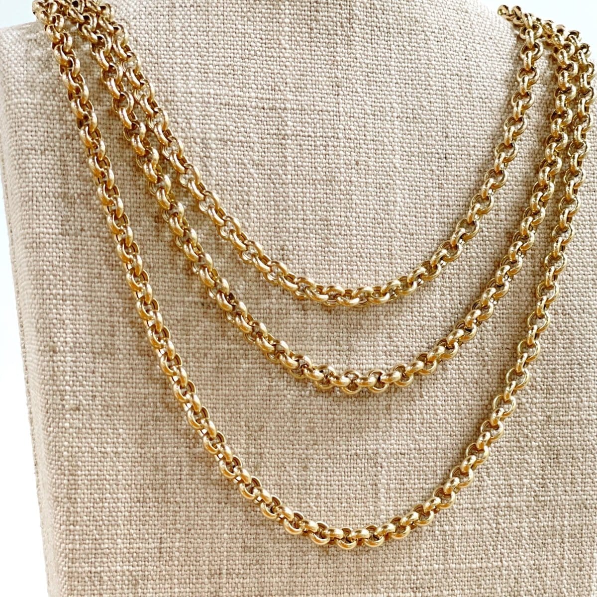 Three yellow gold Rolo Necklaces on a textured beige background.