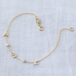 A yellow gold Custom Gold Bracelet - 5 letters, with the letter charms A, S and K and two birthstones on a white fabric background. 