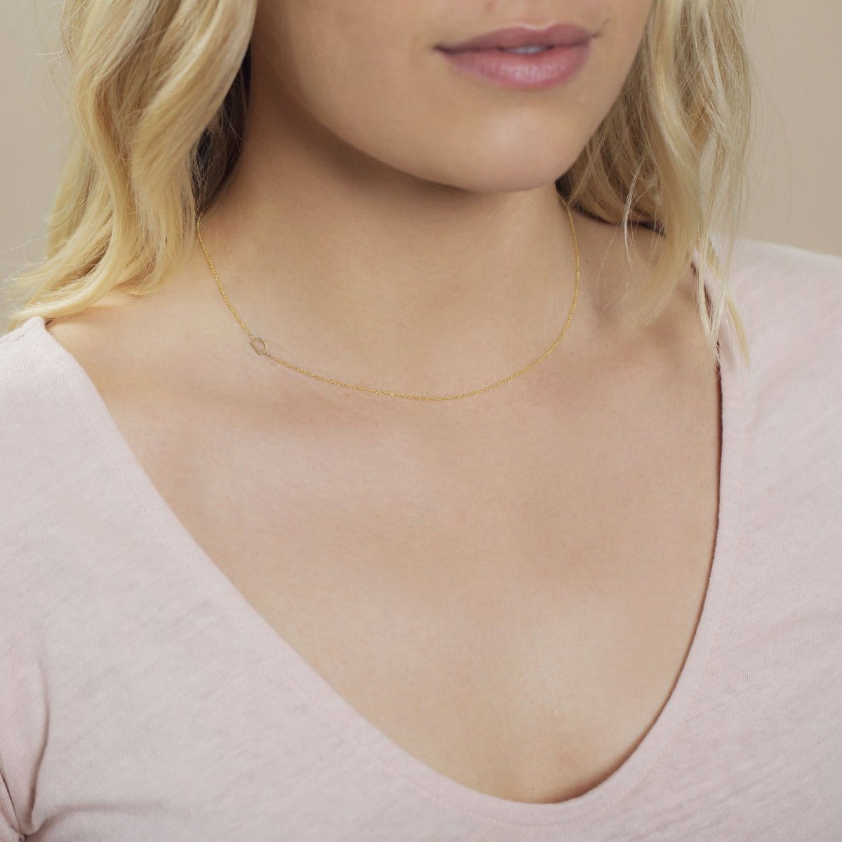 A close-up of a woman's neck wearing a yellow gold necklace with a letter D charm.