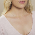 Close-up of a woman's neck wearing a gold necklace with a letter G charm. 