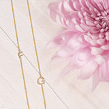 Two yellow gold necklaces with single letter charms, F and G, displayed on a neutral background with a pink flower.