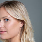 Close-up of a More Love Stud being worn by a blonde woman against a grey background. 