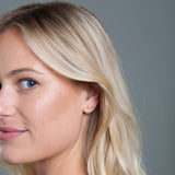 Close-up of a More Love Stud being worn by a blonde woman against a grey background. 