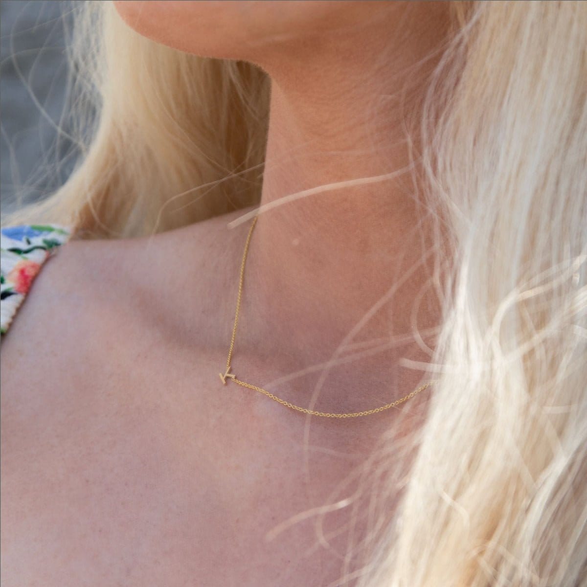 A close-up of a woman's neck wearing a yellow gold necklace with a letter K charm.