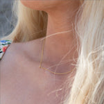 A close-up of a woman's neck wearing a yellow gold necklace with a letter K charm.