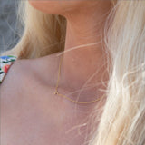 A close-up of a woman's neck wearing a yellow gold necklace with a letter K charm.