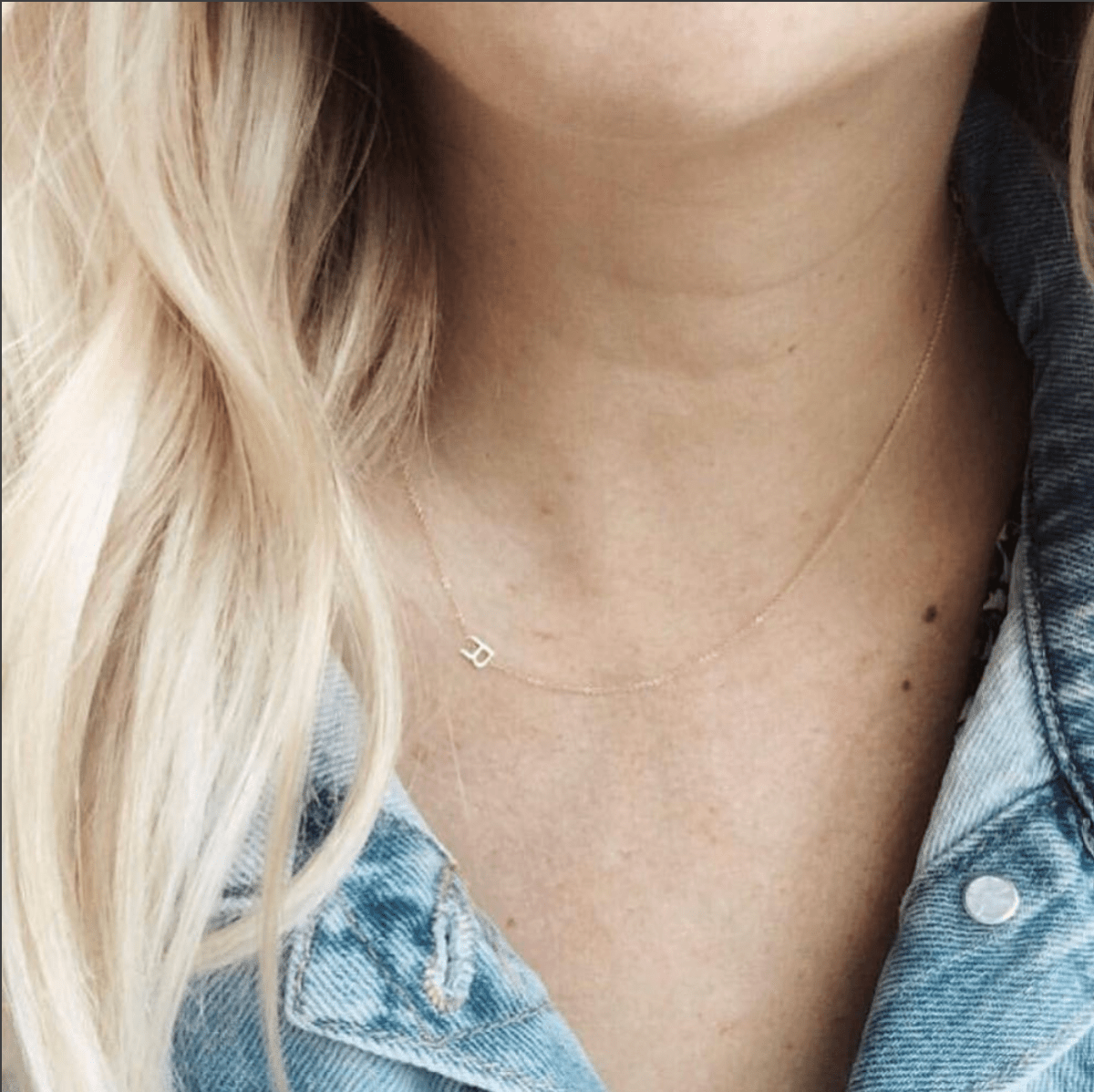 A close-up of a woman's neck wearing a yellow gold necklace with a letter R charm. 