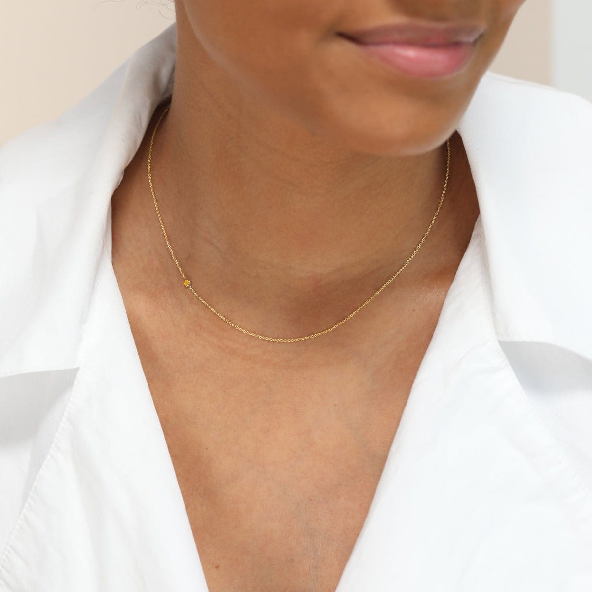 A close-up of a woman’s neck wearing a yellow gold 14K Gold Asymmetrical Birthstone Necklace - Citrine (November), styled in a white shirt. 