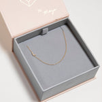 A yellow gold necklace with a pave letter L charm in a jewellery box. 