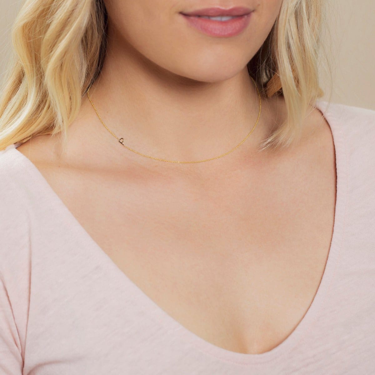 A close-up of a woman's neck wearing a yellow gold necklace with a letter P charm. 