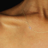 A close up of a woman's décolletage wearing a yellow gold necklace with a letter S charm. 