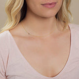 A close-up of a woman's neck wearing a yellow gold necklace with a letter V charm.