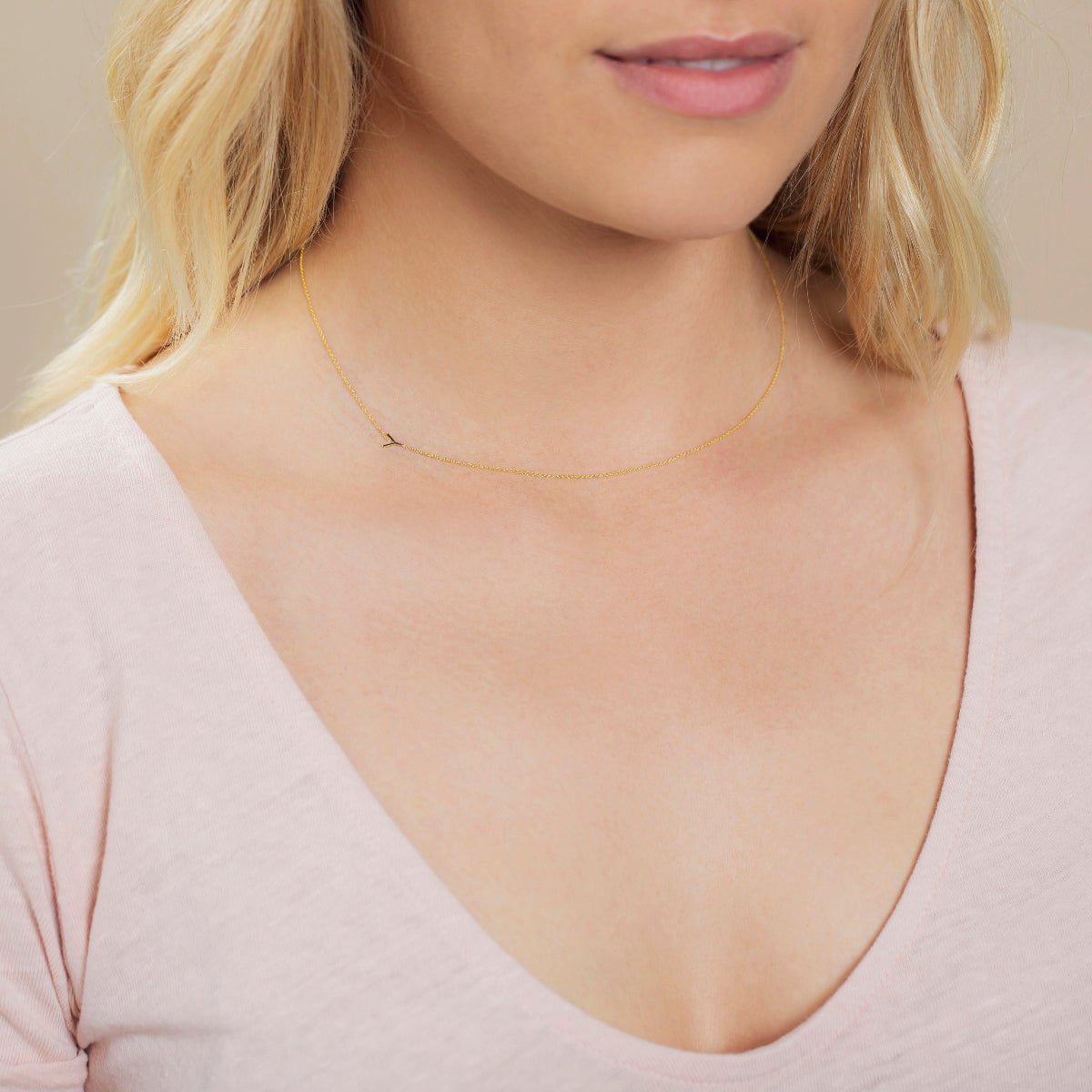A close-up of a woman's neck wearing a yellow gold necklace with a letter Y charm.