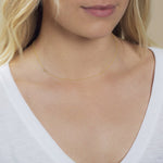 A close-up of a woman's neck wearing a 14k Gold Asymmetrical Number Necklace - 4 in yellow gold, styled with blonde hair and a white top.